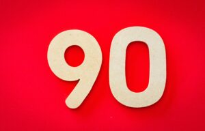 Minimalist depiction of wooden numbers '90' against a vivid red backdrop, capturing simplicity and elegance.